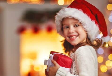 Lachendes Kind hält ein bunt verpacktes Weihnachtsgeschenk