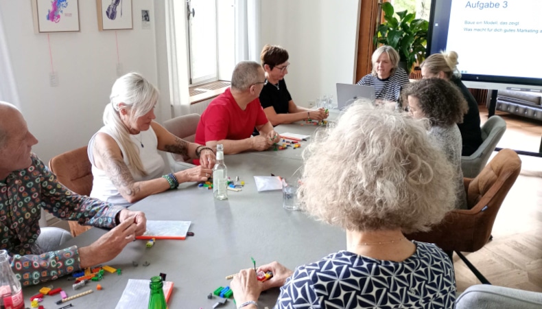 Teilnehmergruppe im Gespräch mit Moderatorin Kerstin Müller beim LEGO® SERIOUS PLAY® Workshop in der Villa Prym