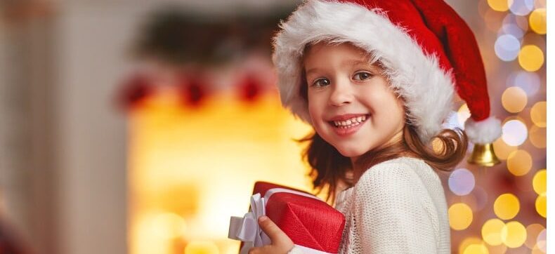 Lachendes Kind hält ein bunt verpacktes Weihnachtsgeschenk