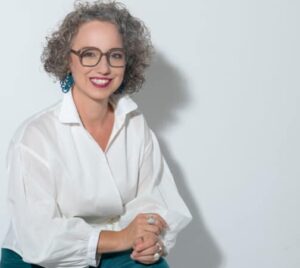Christine Maria Kaltenleitner sitzt im Sommer in weisser Bluse auf einem Stuhl. Referentin des MC Lago Webinars «Der unterschätzte Erfolgsfaktor: Selbstwertgefühl» am 24. August 2026.